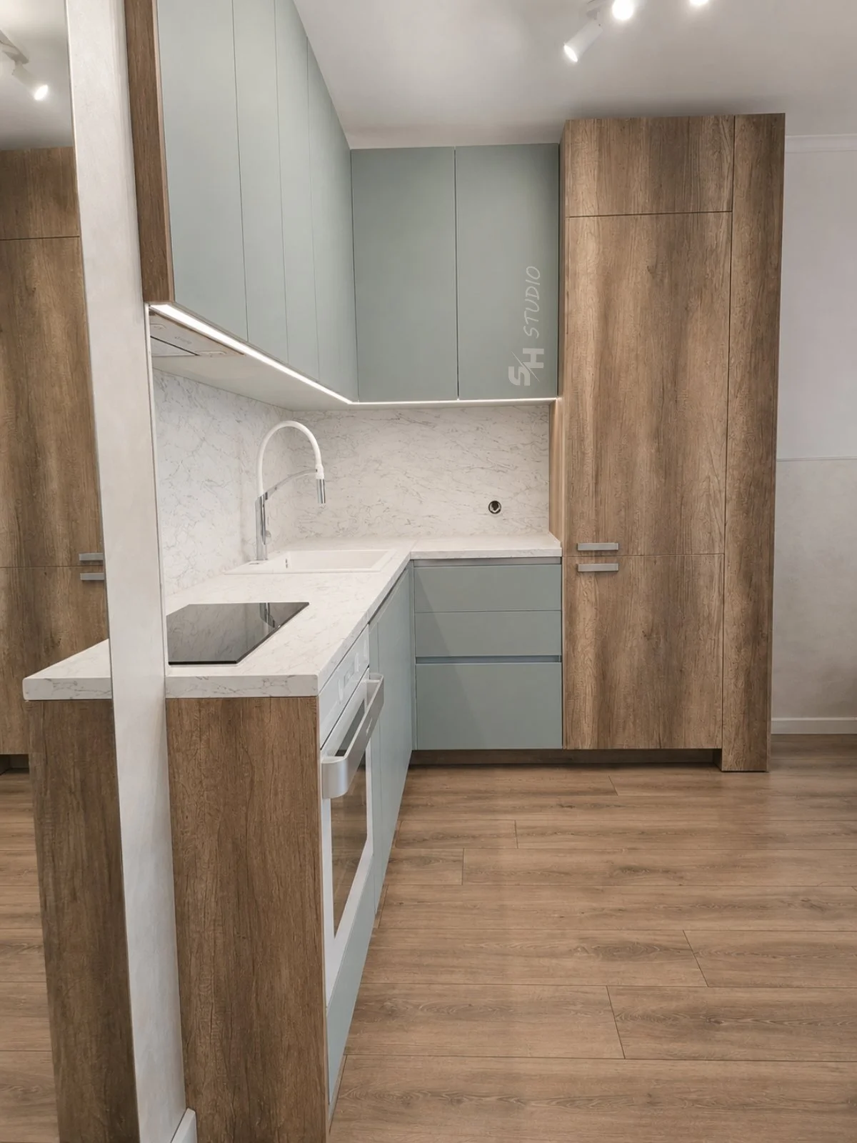 GB Residence — pale blue corner kitchen with oak tall units and induction hob