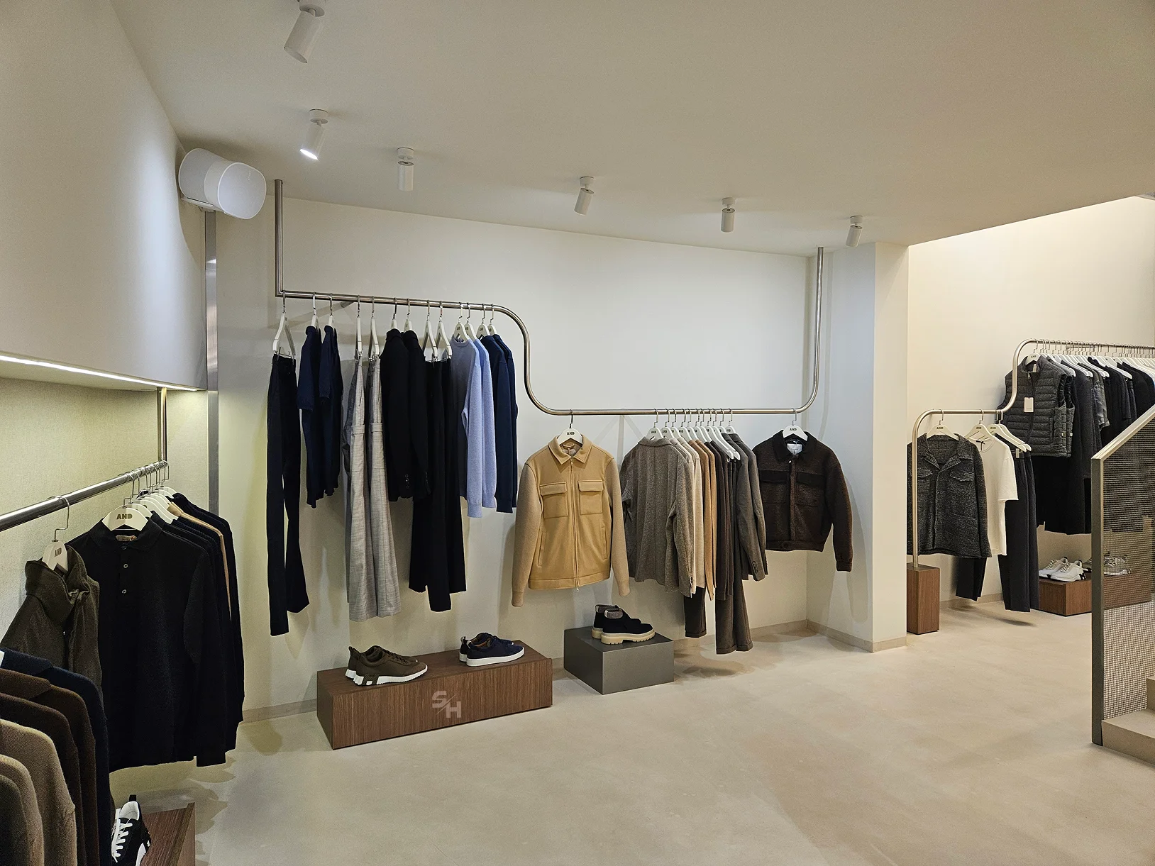 AND menswear store — sales floor with walnut-look wall units, clothing rails and display plinths