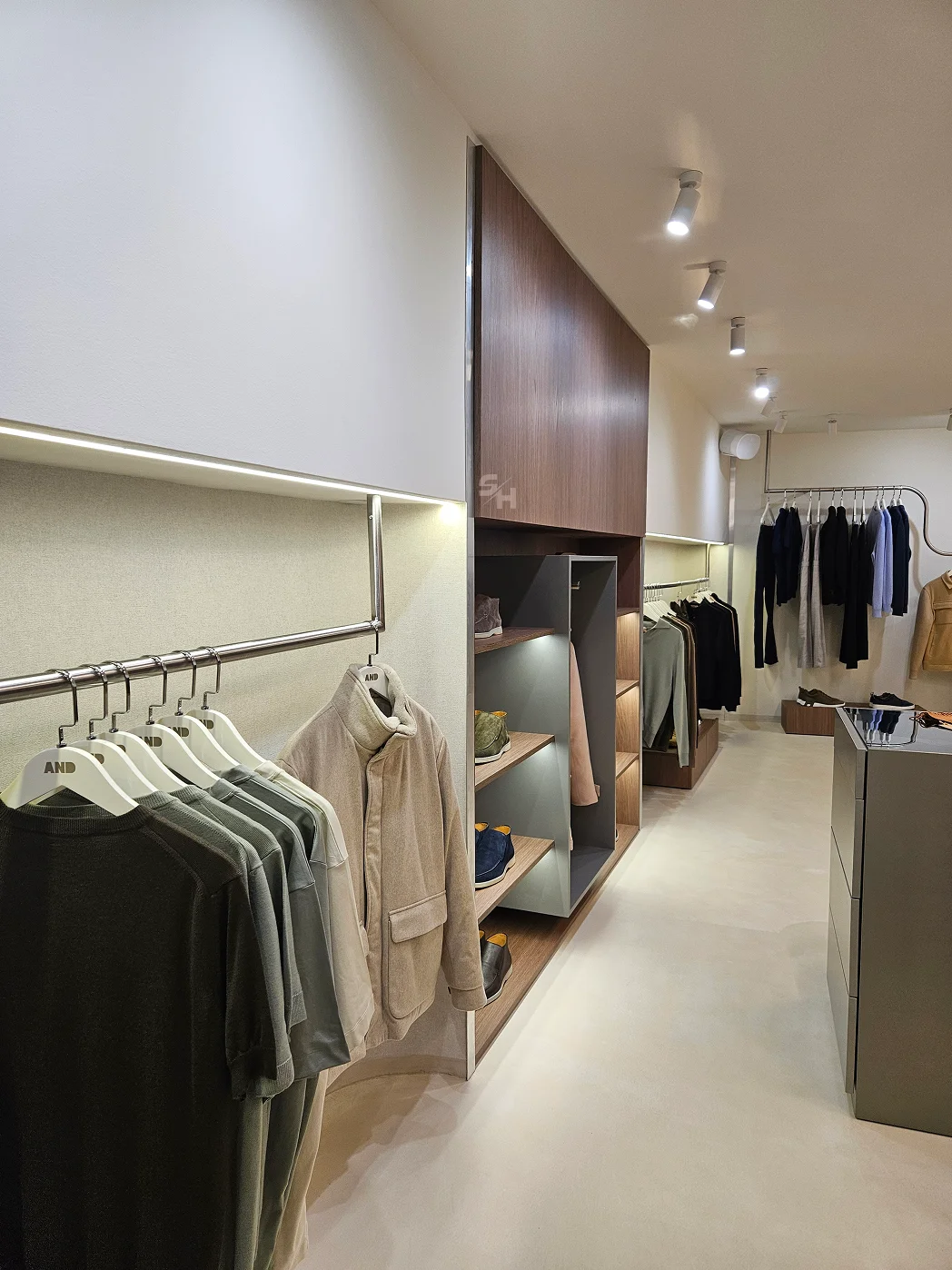 AND menswear store — sales floor with walnut-look wall units, clothing rails and display plinths
