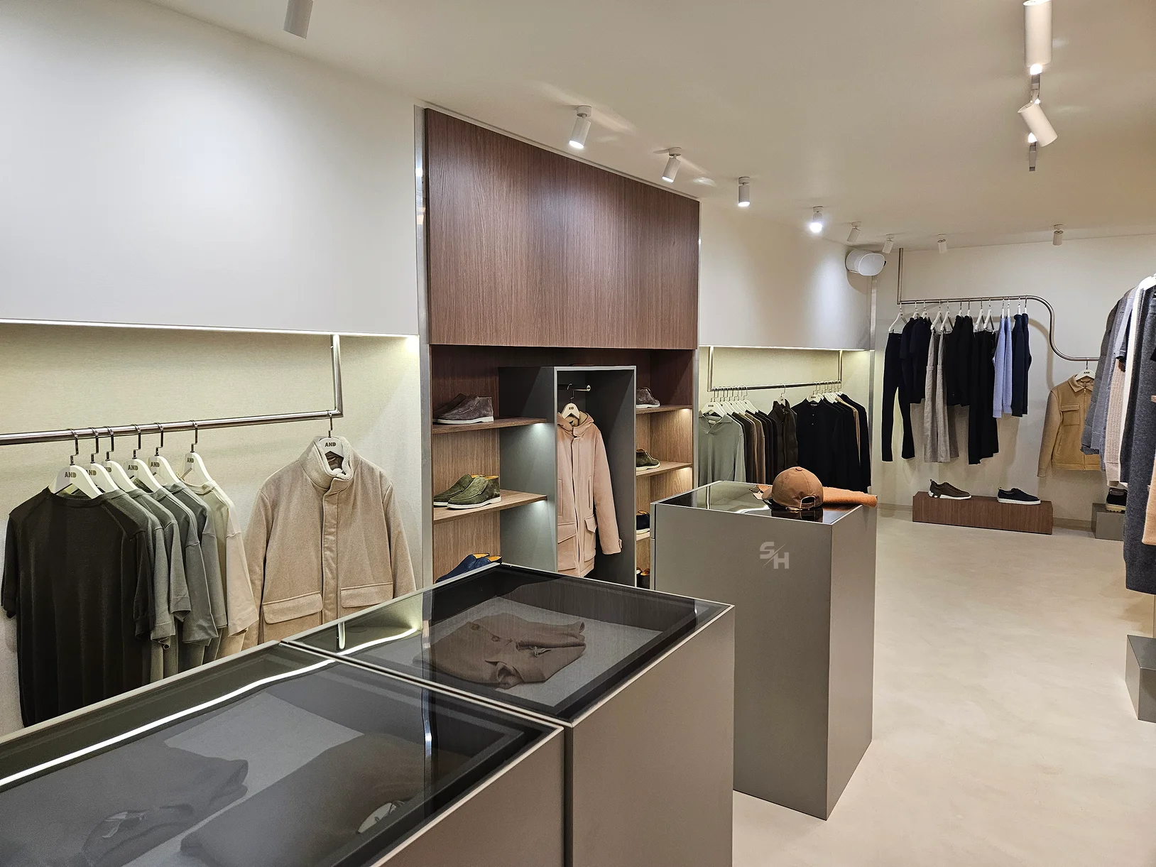 AND menswear store — sales floor with walnut-look wall units, clothing rails and display plinths