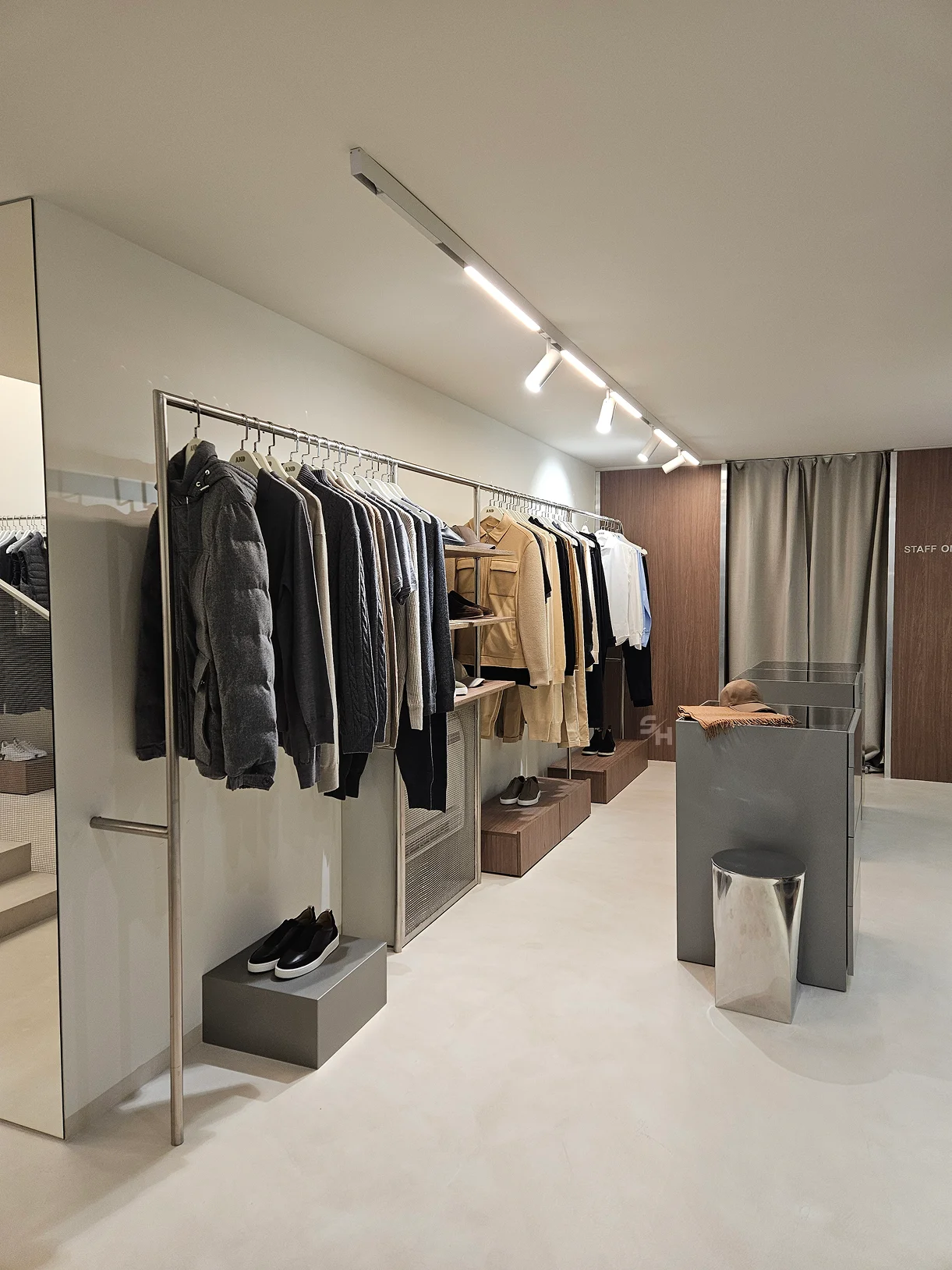 AND menswear store — sales floor with walnut-look wall units, clothing rails and display plinths