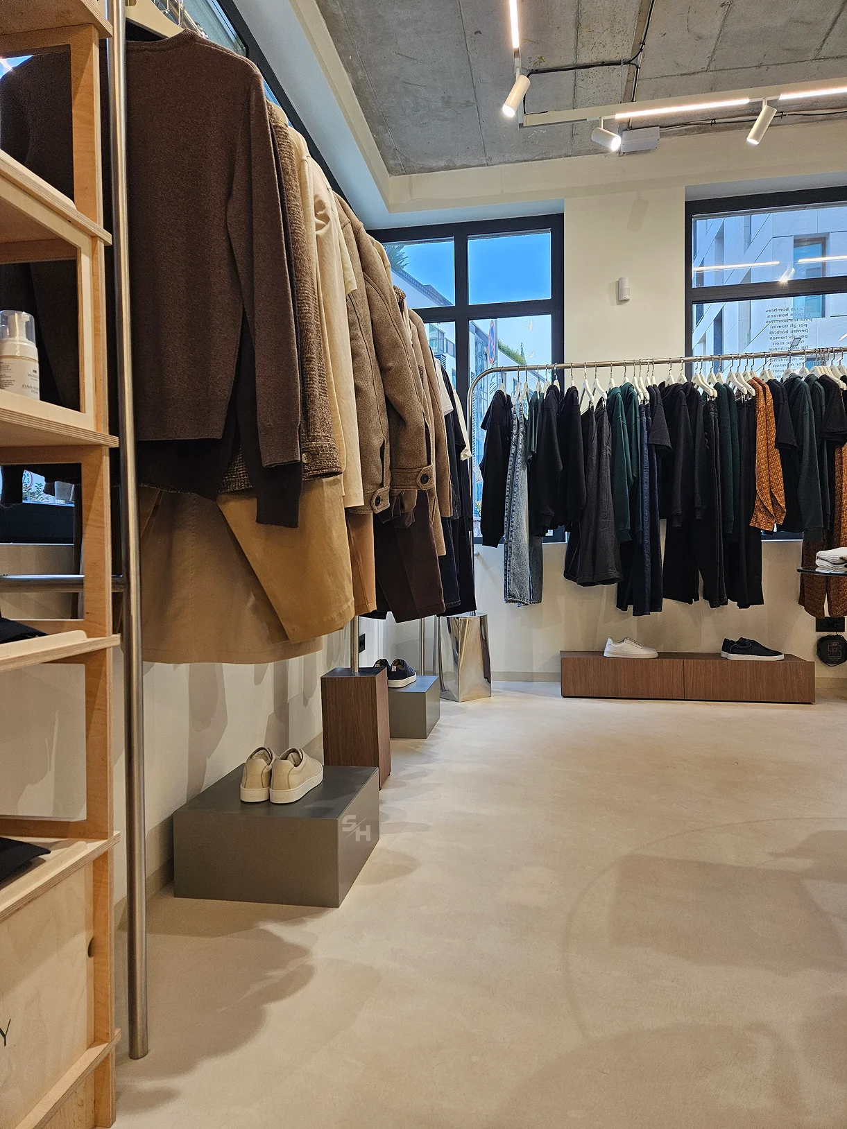 AND menswear store — sales floor with walnut-look wall units, clothing rails and display plinths