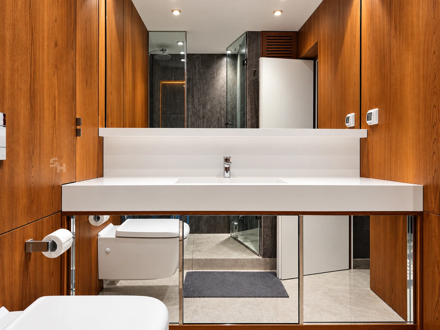 DTDSG — wood-clad bathroom with white solid-surface vanity over mirrored base